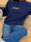 model wearing navy michigan script mock neck by one dna, sitting on a wooden floor