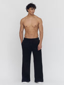 A man on a flat gray background wears black wide-leg sweatpants by One Dna